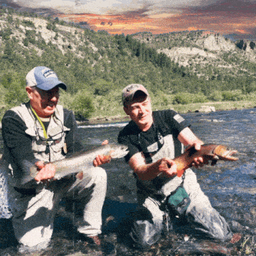 two men are kneeling in a river holding two fish one of whom is wearing a hat that says ' montana '