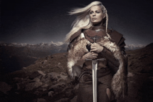 a woman in a fur coat is holding a sword in front of mountains