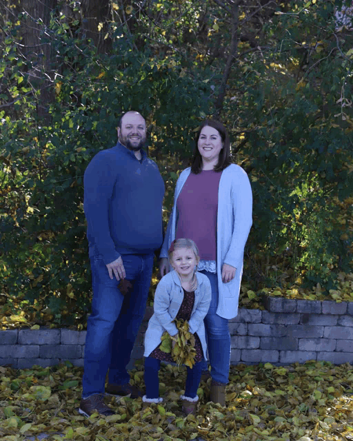 a family posing for a picture with a little girl holding a bunch of leaves