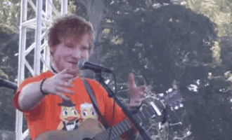 a man is playing a guitar and singing into a microphone while wearing an orange shirt with a duck on it .