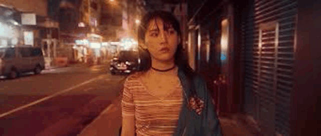 a young woman is walking down a street at night .