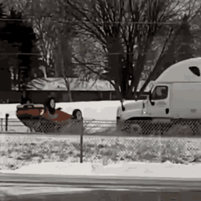 a white semi truck is driving down a snowy road next to a red car that is on the side of the road .