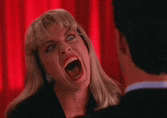 a woman is screaming at a man in front of a red curtain in a room .