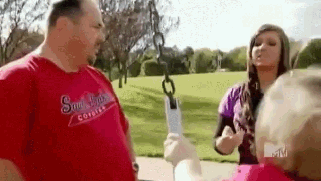 a man in a red shirt is talking to a woman in a pink shirt while standing next to a swing .