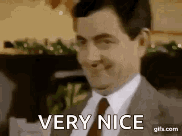 mr bean is wearing a suit and tie and smiling while saying `` very nice '' .