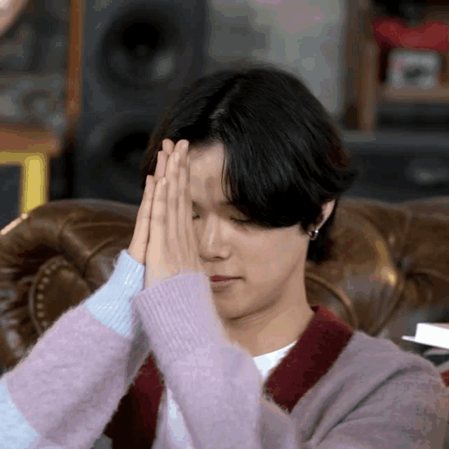 a young man is sitting on a couch with his hands folded in front of his face