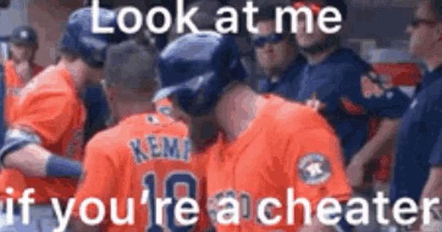 a group of baseball players are standing next to each other in a dugout and talking to each other .