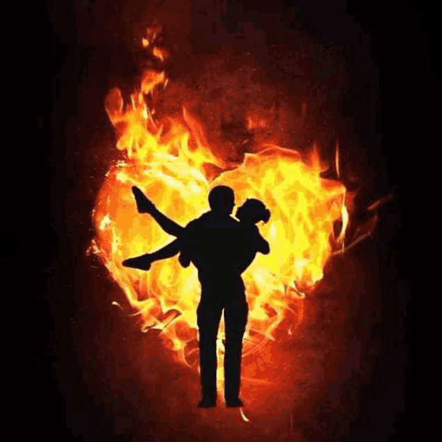 a man is carrying a woman in his arms in front of a heart of fire .