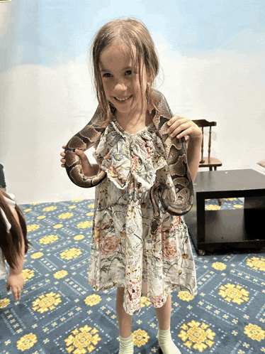 a little girl in a floral dress holding a snake