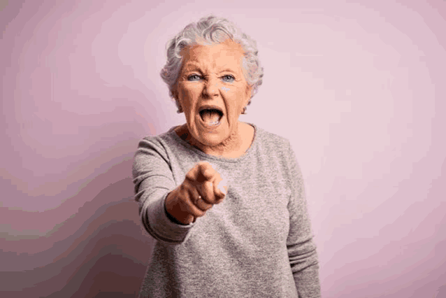 an elderly woman is screaming and pointing at the camera with her mouth open .