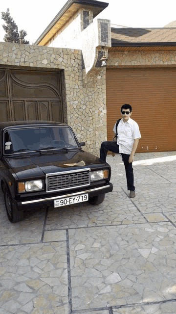 a man stands next to a black car with a license plate that says 90-ey-719