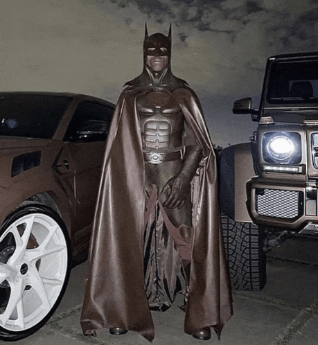 a man dressed as batman stands in front of a car