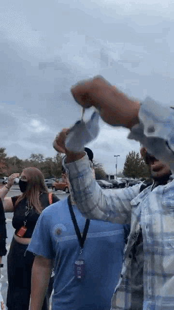 a man in a plaid shirt is holding a mask in his hand while standing in a parking lot .