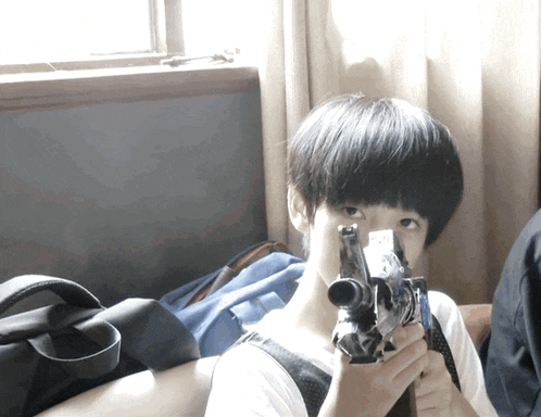 a young boy is holding a camera in front of his face and looking at it