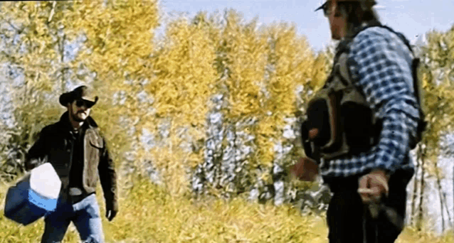 two men in cowboy hats are standing in a field talking