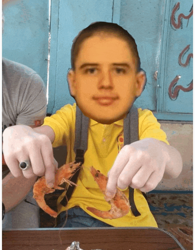 a man in a yellow shirt is holding shrimp in front of his face