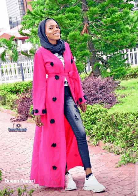 a woman wearing a pink coat with black flowers on the sleeves and a black hijab