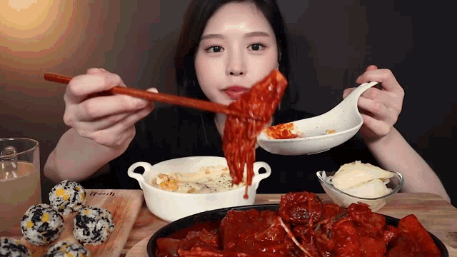 a woman is eating a meal with a spoon and chopsticks with a bowl of rice balls in the background