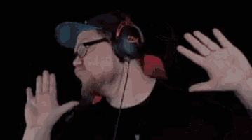 a man wearing headphones and glasses is making a funny face with his hands in the air .