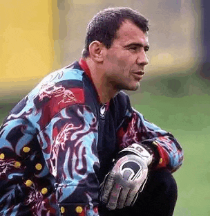 a soccer goalie wearing a colorful jacket and gloves is kneeling down on the field .