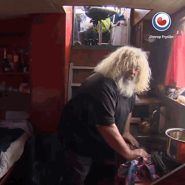 a man with blonde hair and a beard is washing dishes in a kitchen with omrop fryslan on the bottom right