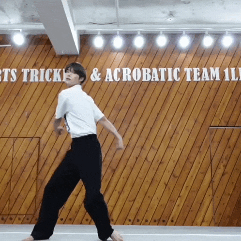 a man is dancing in front of a wooden wall that says ' tricks & acrobatic team ' on it