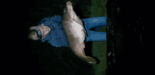 a man wearing a headlamp is holding a large fish in his hands