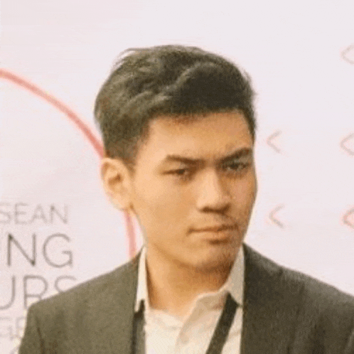 a young man wearing a suit and tie is standing in front of a white wall .