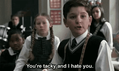 a young boy in a school uniform is standing in front of a group of children in a classroom and talking to them .