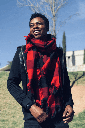 a man wearing a black jacket and a red plaid scarf smiles