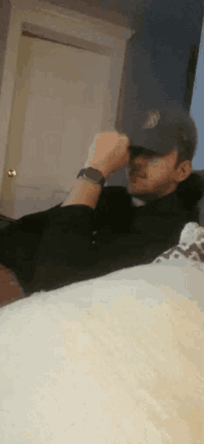 a man wearing a hat and a watch is laying down on a bed