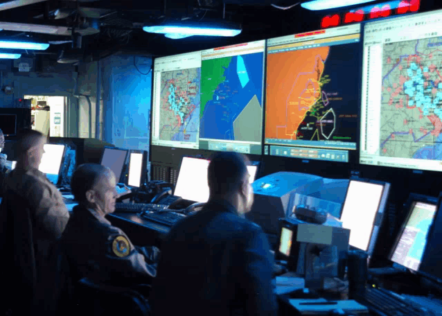 a group of men are sitting in front of computer monitors and one of them has a patch on his chest that says ' army '