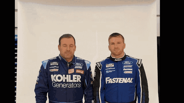 two men standing next to each other with one wearing a fastenal jacket