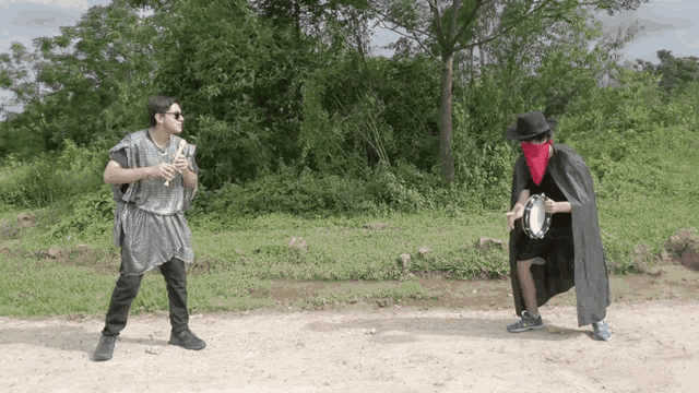 a man playing a flute and a man playing a tambourine are standing next to each other on a dirt road