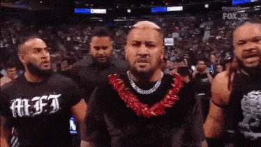 a group of men standing next to each other in a stadium . one of the men is wearing a lei around his neck .