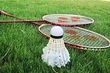 A shuttlecock and two badminton rackets are laid out on grass.