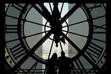 Silhouettes of two people in front of the inside of a large, clear clock overlooking a city.