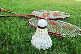 A shuttlecock and two badminton rackets are laid out on grass.