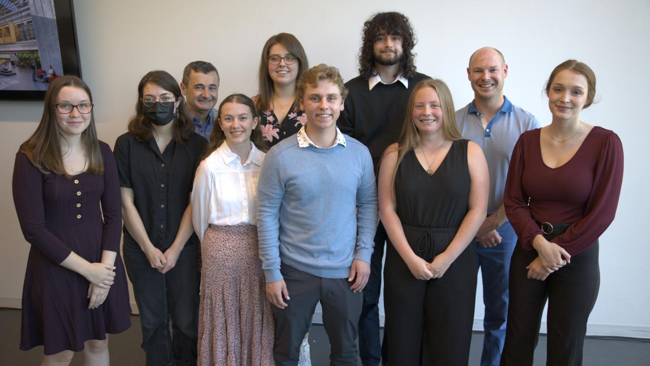 A group of ten people standing together and smiling towards the photographer.