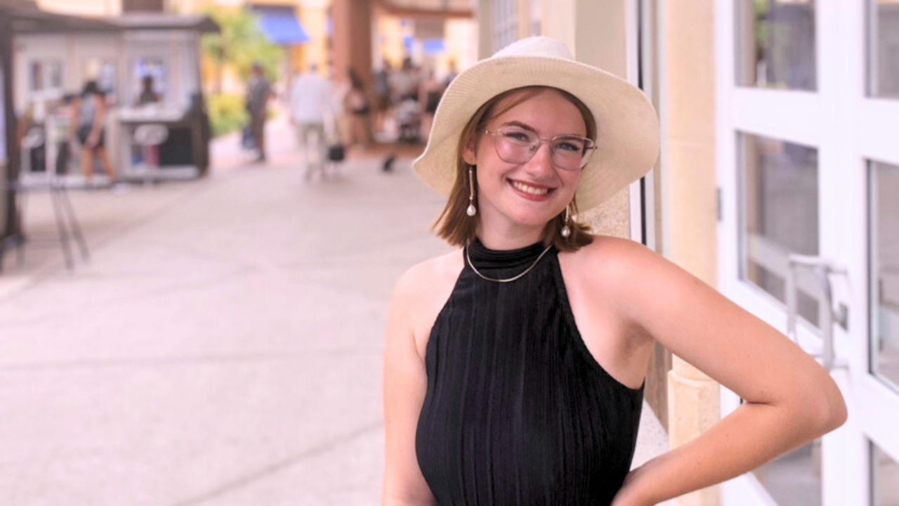 Rory Duffy is standing outside. She is wearing a black shirt, a necklace, pearl earings, and a light-coloured sun hat.