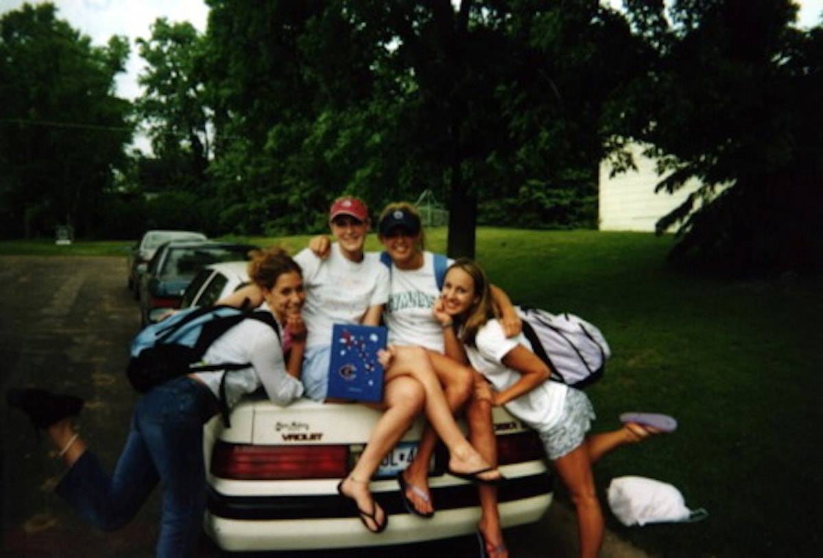 Four women sitting on the back of a vehicle.