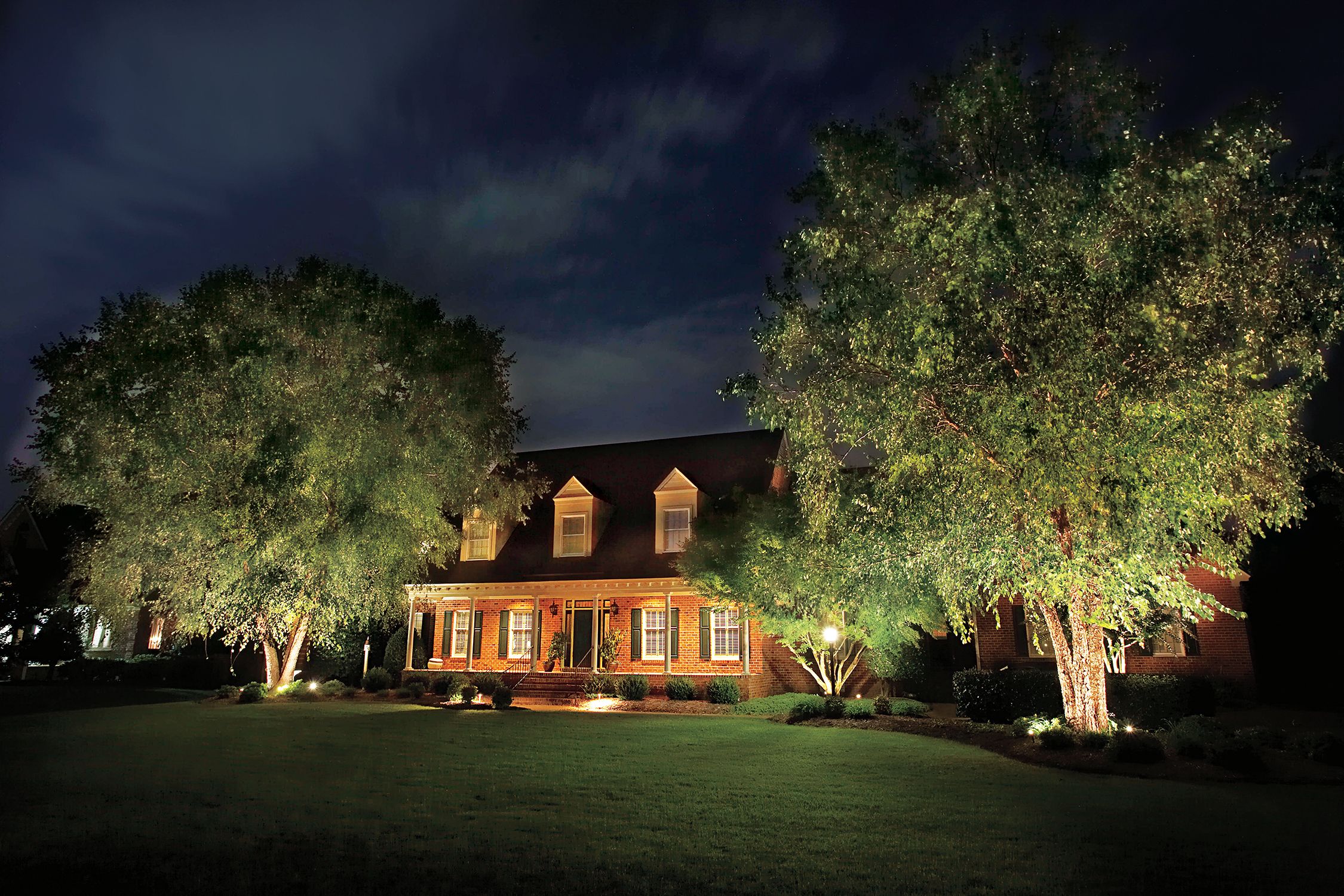 A landscape lighting system casting light on a tree and home at night.