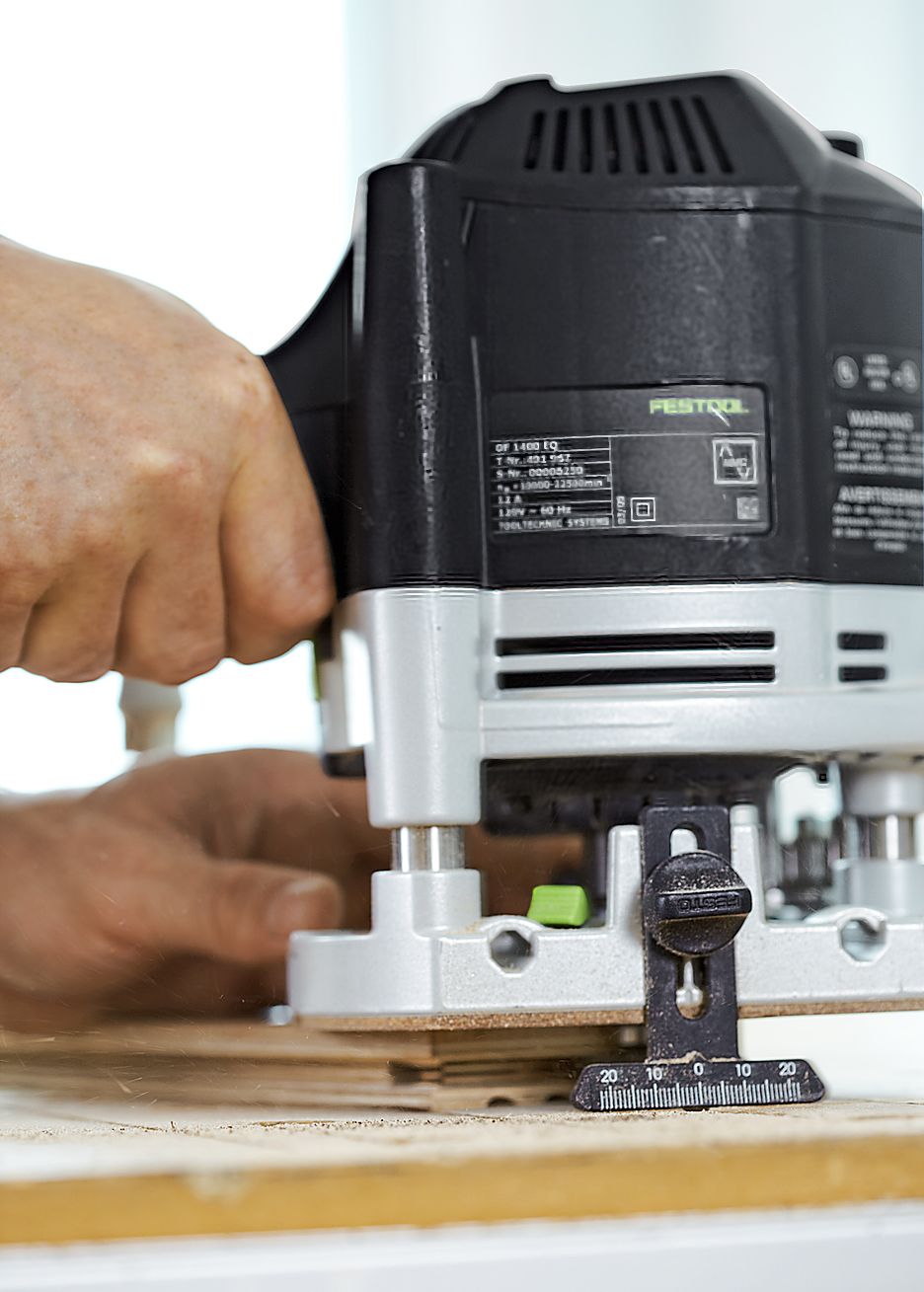 A person adds grooves to the ends of the herringbone floor planks with a router.