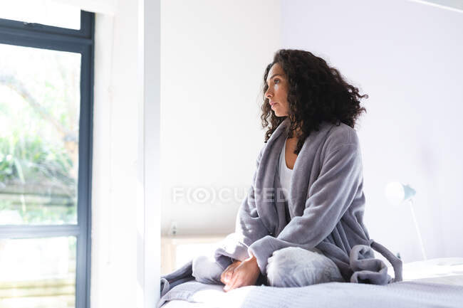 Glücklich nachdenkliche Mischlingshündin, die auf dem Bett sitzt und durch das Fenster schaut. Lebensstil und hochwertige Zeit zu Hause verbringen. — Stockfoto