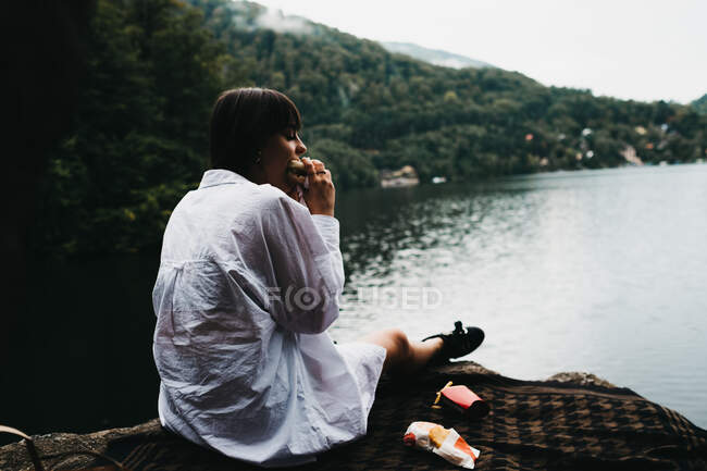 Frau isst Hamburger in der Nähe von See und Bergen — Stockfoto