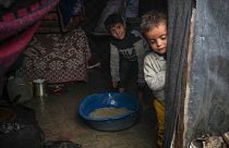 Brothers Belal, 5, and Mohammed Hamad, 7, collect water from their flooded family tent after overnight rainfall at the refugee tent camp, 31 December 2024 