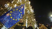 A man with an EU flag stands next to a Christmas Tree in a street decorated for Christmas and the New Year festivities outside of the Georgian arliament, in Tbilisi