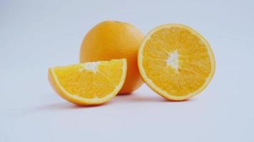 Zoom in to cut in half and slice a ripe orange fruit with golden yellow peel. Isolated on white background with shadow. video