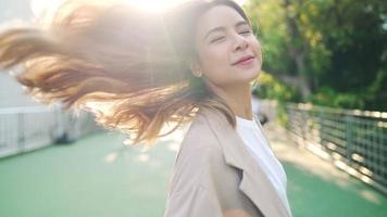 cerca de una joven mujer alegre en la escena del parque del paso elevado de la ciudad, una mujer hermosa con el pelo rubio largo y descolorido gira alrededor de sí misma felizmente, la llamarada del sol ilumina, la naturaleza y la belleza del video en cámara lenta