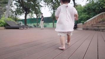 Asian little girl walking toward father in the public park, baby caring inside parents watch, toddler first step, beginning of new life, cute innocence purity, view from behind of young little toddler video